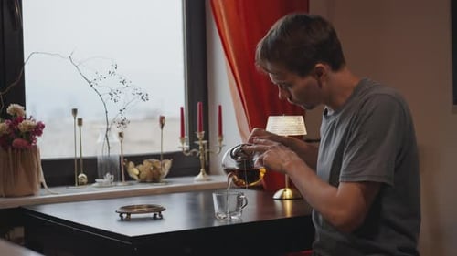 Un homme à la maison à une table près de la fenêtre sert du thé