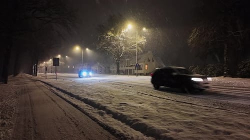 Multiple cars driving over a speed bump on a long snow covered road on a cold winter night