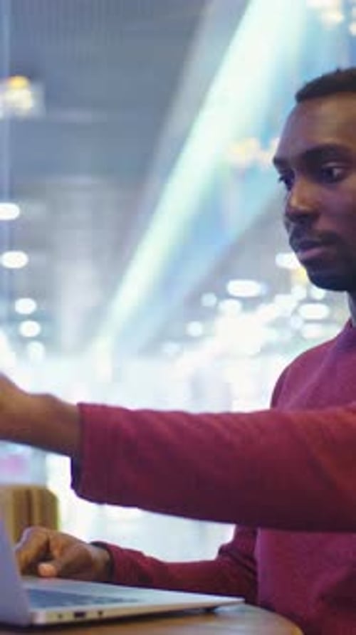 Homme afro-américain travaillant sur un ordinateur portable dans un café moderne avec éclairage ambiant lumineux et décor