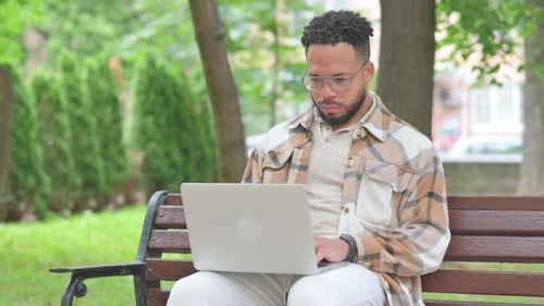 Man Works on Laptop Sitting on Park Bench