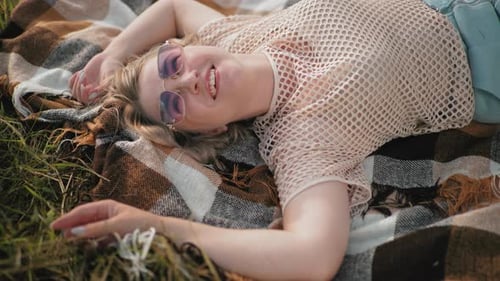 Smiling Woman in Net Top Sunglasses Lying on Blanket in Grassy Field