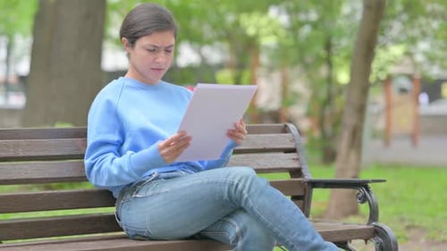 Outdoor Sitting Indian Woman Shocked while Reading Documents