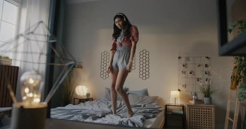 Beautiful Asian Girl in Pajamas Listening to Music with Headphones Dancing on Bed Having Fun in