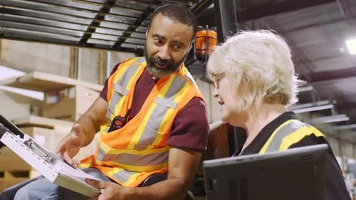 Distribution Warehouse Owner Discussing Paperwork with Forklift Driver Adult