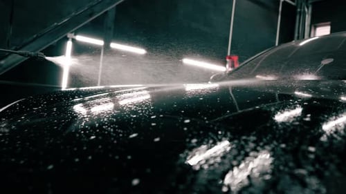 close-up A male car wash employee applies car wash detergent to a black luxury car using spray gun