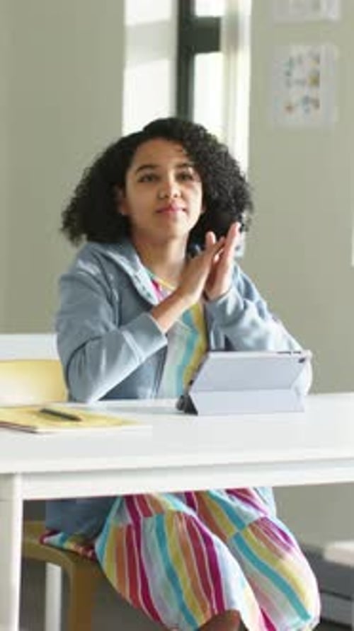 Vertical video: Clapping student in blue hoodie starting after hands meet during class, with tablet