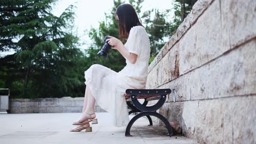 Woman Sits on Bench Reviewing Photos on Camera