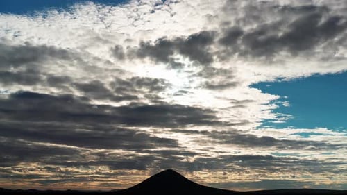A colorful sunset cloudscape above the silhouette of a butte in the Mojave Desert in this wide angle