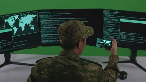 Soldat asiatique travaillant avec un téléphone portable tout en écrivant du code avec plusieurs écrans en vert
