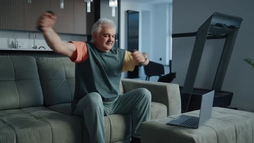 GrayHaired Man With Moustache Training Alone At Home Watching Online Workout At Laptop Screen