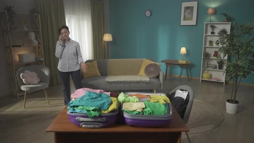 Video of a Brunette Middleaged Woman Having a Call on the Background While Packing a Suitcase Laying