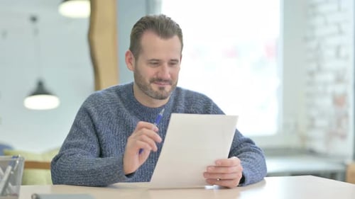 Middle Aged Man Celebrating Success while Reading Documents in Office