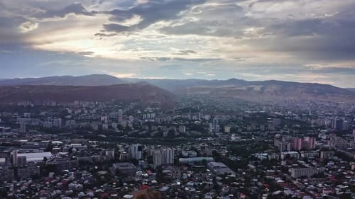Aerial view of Tbilisi among hills and mountains under sunset cloudscape