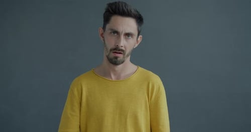 Zeitlupenporträt eines unglücklichen und verärgerten jungen Mannes, der Selbstmord begeht, mit Kopfgeste auf Grau
