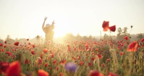 Brunette Woman in a Yellow Dress and Straw Hat Dancing Happy in Poppy Field at Sunrise