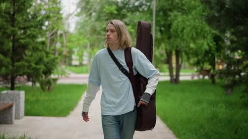 Indie Artist on Peaceful Walk Caucasian Musician Carrying Guitar Heading to Practice Blonde