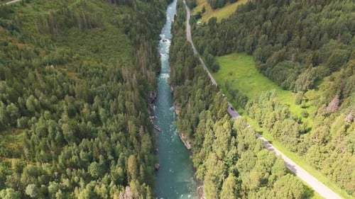 Aerial view of a river flowing through a lush, forested valley with a winding road running alongside