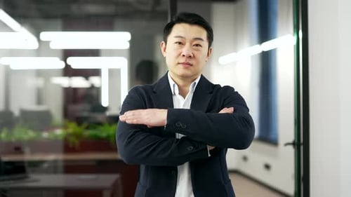 Porträt eines glücklichen asiatischen Geschäftsmannes in einem formellen Anzug, der mit verschränkten Armen in einem Geschäft steht