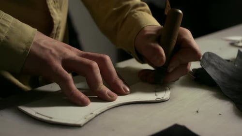 Artisan man working leather with awl in bright leathercraft workshop studio