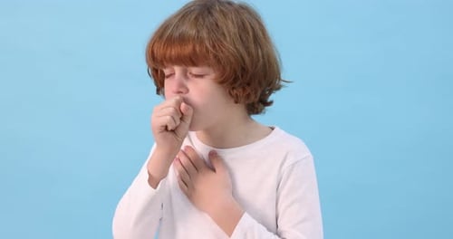 Little boy coughing on light blue background. Cold symptom