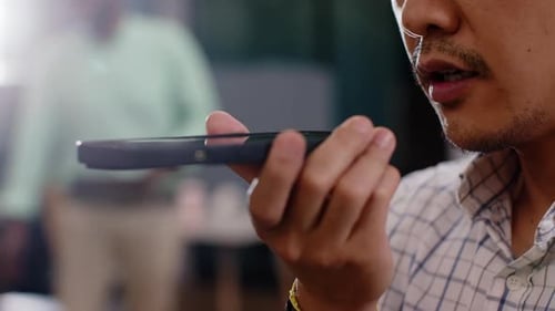 Speaking into smartphone, man using voice command feature in office setting