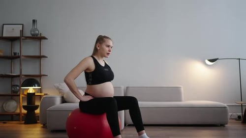 Femme enceinte athlétique s'entraînant avec une balle de fitness à la maison, s'étirant pour soulager les douleurs vertébrales