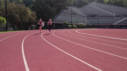 Two athletes running on a curved track with a stadium visible in the background, sunny day
