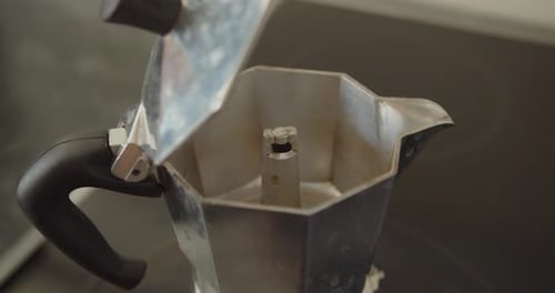 Primer plano de una olla de moka en un plato caliente en la cocina. Una mano caucásica abre la tapa de la olla, c.