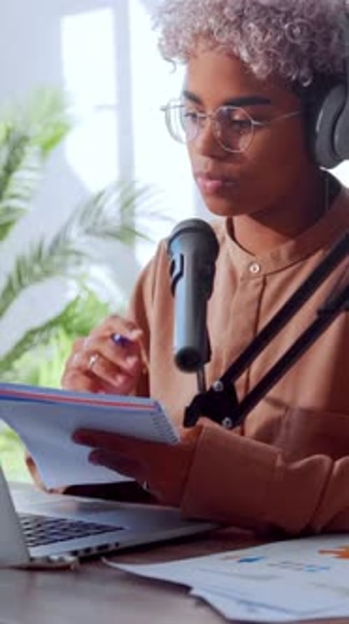 Young African American Woman in Glasses and Headphones Writes in Her Notebook