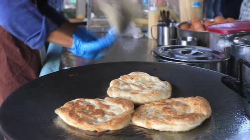 Street food vendor is preparing the dough and pan-frying paratha roti in hot oil until crispy on the