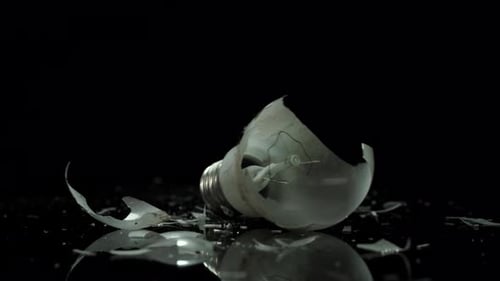 Broken incandescent lamp with a tungsten filament wire and glass pieces, bulb closeup
