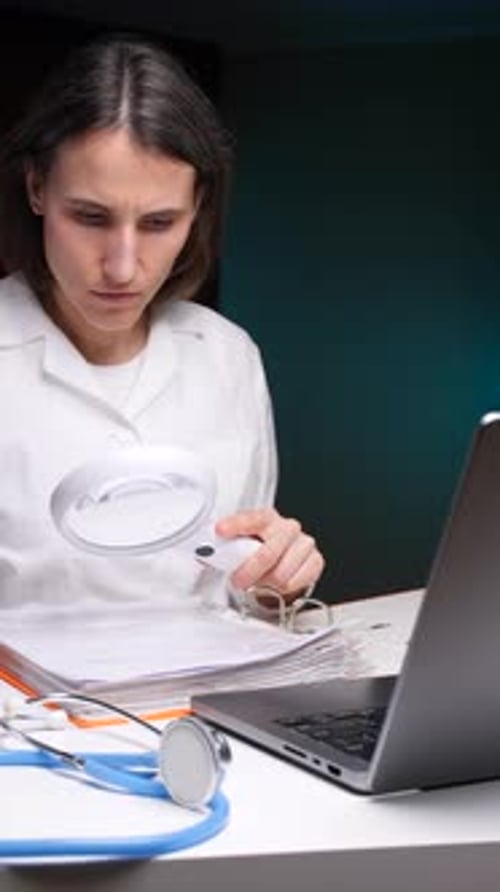 Vertical Video Doctor Examining Medical Records with Magnifying Glass in Dark Room