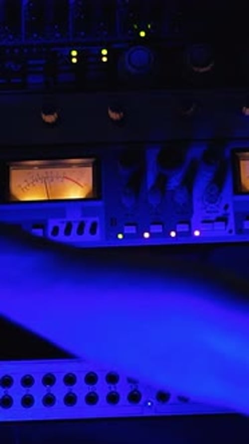 Studio recording equipment in the blue light. Male audio engineer's hand working on the stereo panel