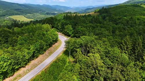 Flight over the green slopes of wooded mountains. A highway is built through the lush forests.