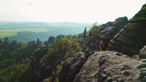 Woman hiking on the edge of a rocky cliff in Schrammsteine Elbe Sandstone Mountains in Germany with