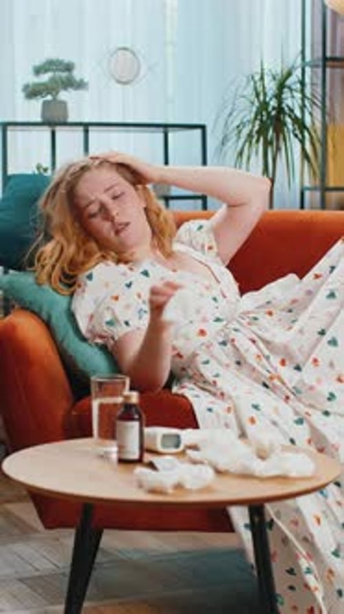 Une femme malade souffrant de rhume ou d'allergie, allongée sur le canapé de la maison, éternue avec de la morve