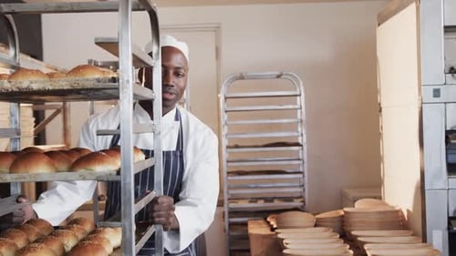 Fröhliche, vielfältige Bäcker, die in der Bäckereiküche arbeiten und Backbleche mit Brötchen in Zeitlupe halten