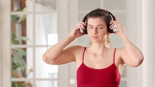 A Woman in Red Sportswear Puts on Headphones and Starts Her Morning Workout A Young Brunette Listens