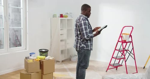 Man with Tablet Standing in a Room with Painting Supplies
