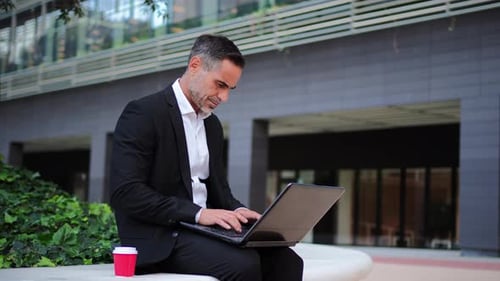 Individual Portrait of a Mature Businessman Sitting Outside in the Financial District Working with a