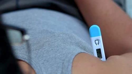 Top View of Man holds a digital thermometer underarm to measure the body temperature for fever.