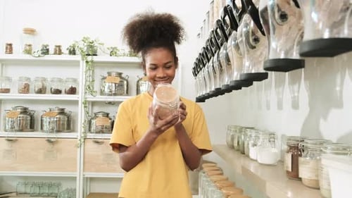 A young woman shops in refill store with reusable and zero-waste containers.