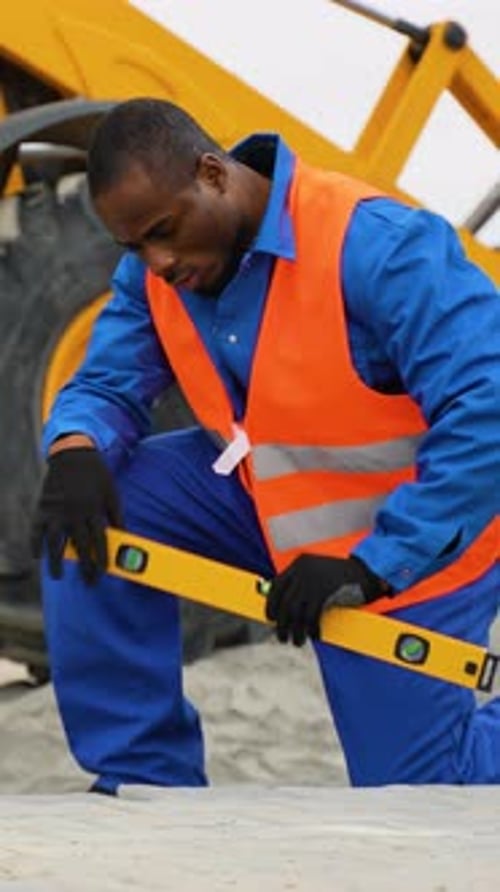 African American Worker Installing Paving Stones Near Heavy Machinery