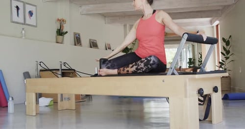 Fit senior caucasian woman stretching on reformer in pilates studio, unaltered, in slow motion