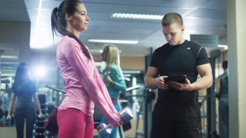 Attractive fit sporty girl is exercising squats with dumbbell in the gym.