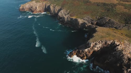 Aerial view of rugged coastal cliffs meeting the deep blue Atlantic, with waves crashing into rocky