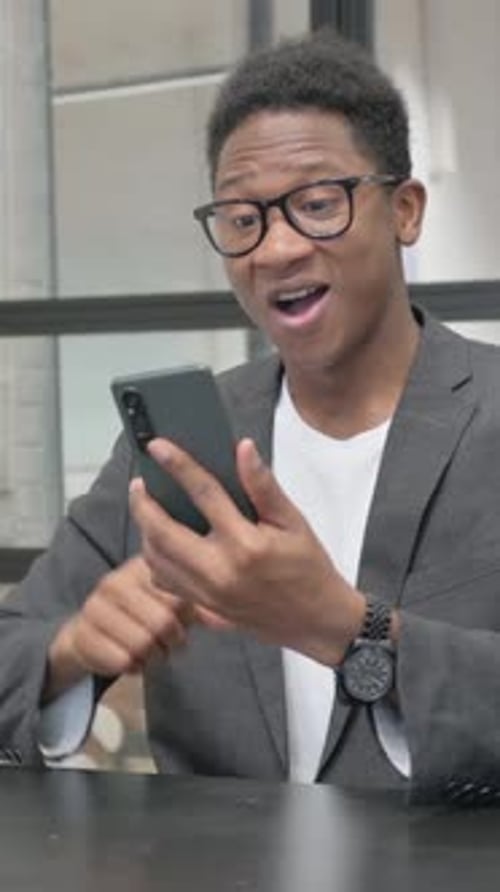Vertical, Young African Man Celebrating Success on Phone in Office