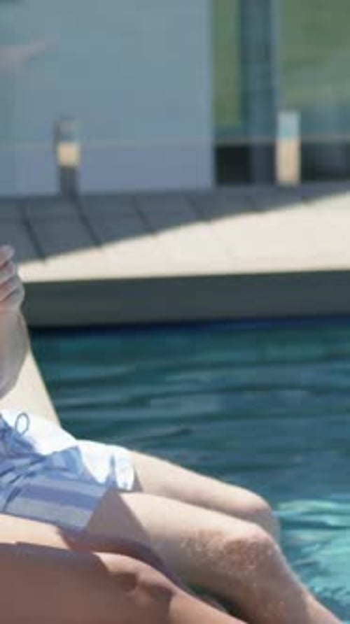 Vertical video: Handing two glasses, man in striped trunks toasting woman in one-piece at pool