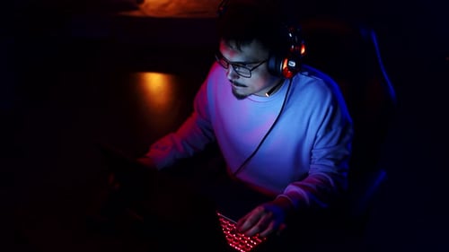 Man with Headphones is Playing Videogames on Laptop in Room with Neon Lighting Top View