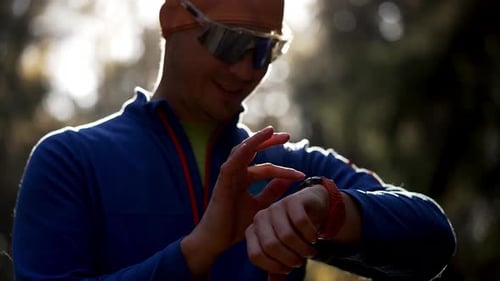 Fit Man in Athletic Attire Checking His Exercise Stats on a Smart Watch Postrun in a Park with a